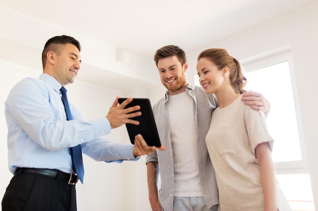 Foto hipoteca, pessoas e conceito imobiliário - casal feliz e corretor imobiliário com tablet pc em casa nova