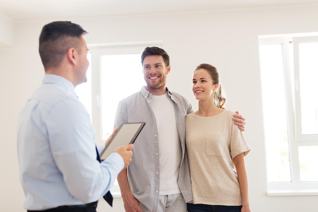 Foto hipoteca, pessoas e conceito imobiliário - casal feliz e corretor imobiliário com tablet pc em casa nova