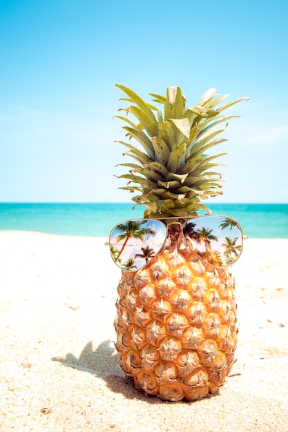 Hippie-Ananas mit Sonnenbrille an einem sandigen Strand.