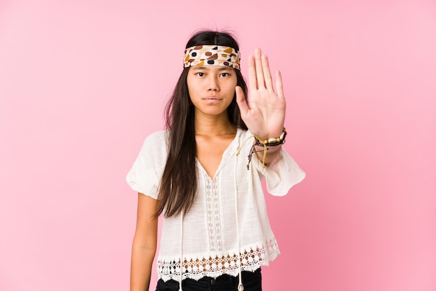 Foto hippie chino joven aislado de pie con la mano extendida que muestra la señal de stop, impidiéndole.