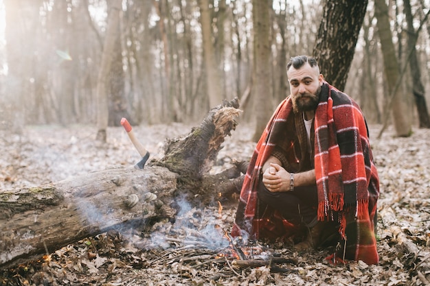 Hippie im Plaid, das nahe Lagerfeuer sitzt