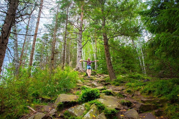 Hippie-Mädchen in den Bergen. Stilvolle Frau mit Strohhut und kariertem Hemd im Wald. Fernweh-Konzept. Reisen und Wandern im Sommer. geheimnisvolles Holz. Schöne Natur.