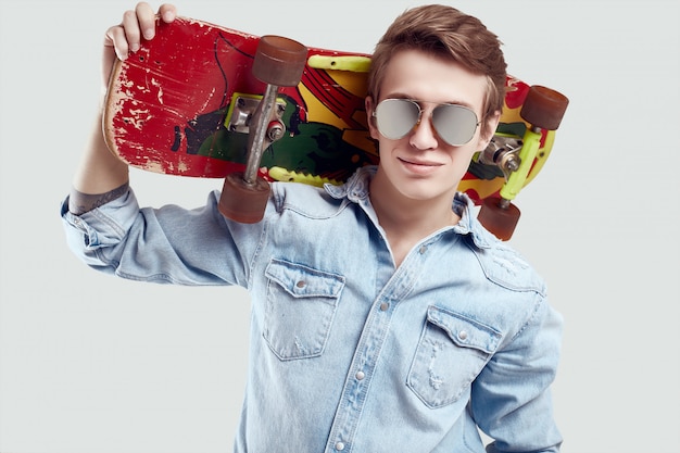 Hippie-Mann in der Sonnenbrille und in Jeansjacke, die mit Skateboard aufwerfen