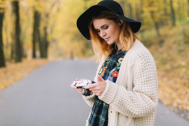 Hippiemädchen mit alter Kamera in einer gestrickten Strickjacke und in einem Hut geht Herbstpark.