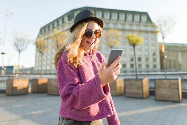 Hipster adolescente menina de chapéu e óculos com telefone celular
