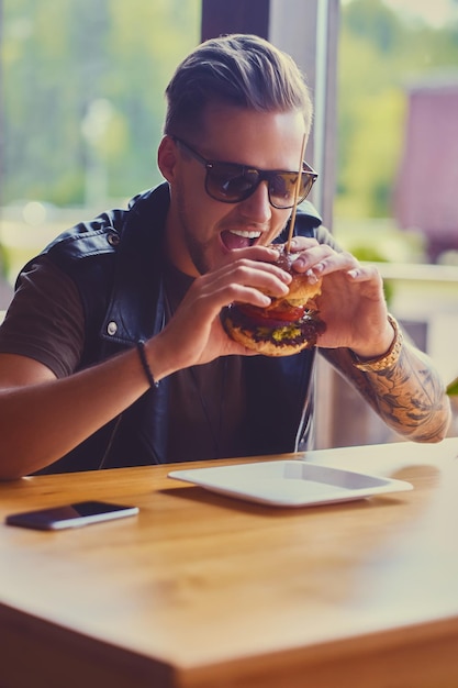 Hipster atractivo vestido con chaqueta de cuero comiendo una hamburguesa vegana.