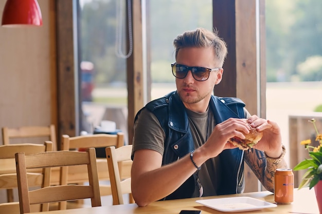 Hipster atractivo vestido con chaqueta de cuero comiendo una hamburguesa vegana.