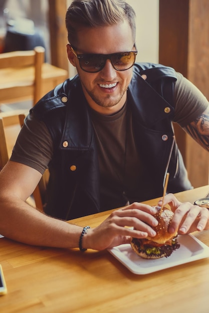 Hipster atractivo vestido con chaqueta de cuero comiendo una hamburguesa vegana.