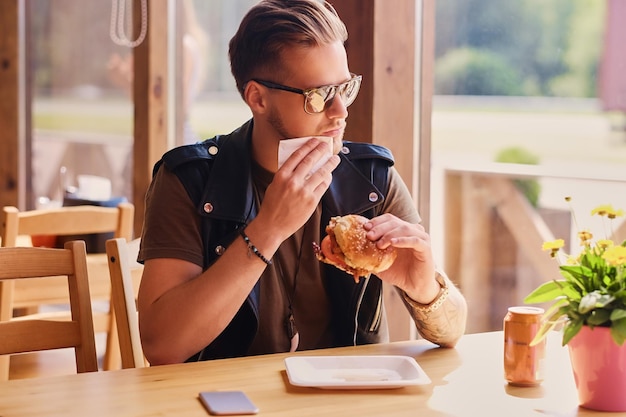 Hipster atraente vestido com jaqueta de couro comendo um hambúrguer vegano.