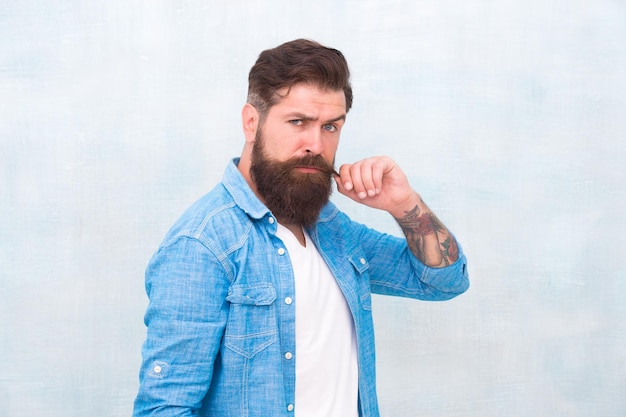 Hipster con barba y bigote usar camisa de mezclilla Concepto de belleza masculina Brutal hombre hipster guapo sobre fondo de pared gris Hombre barbudo estilo hipster de moda Peluquería Macho bien arreglado