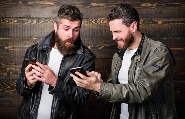 Hipster barbudo brutal de homens em jaquetas de couro da moda usam internet móvel Negócios online Tecnologia moderna Homens com smartphones navegando na internet Aplicativo de negócios de internet móvel