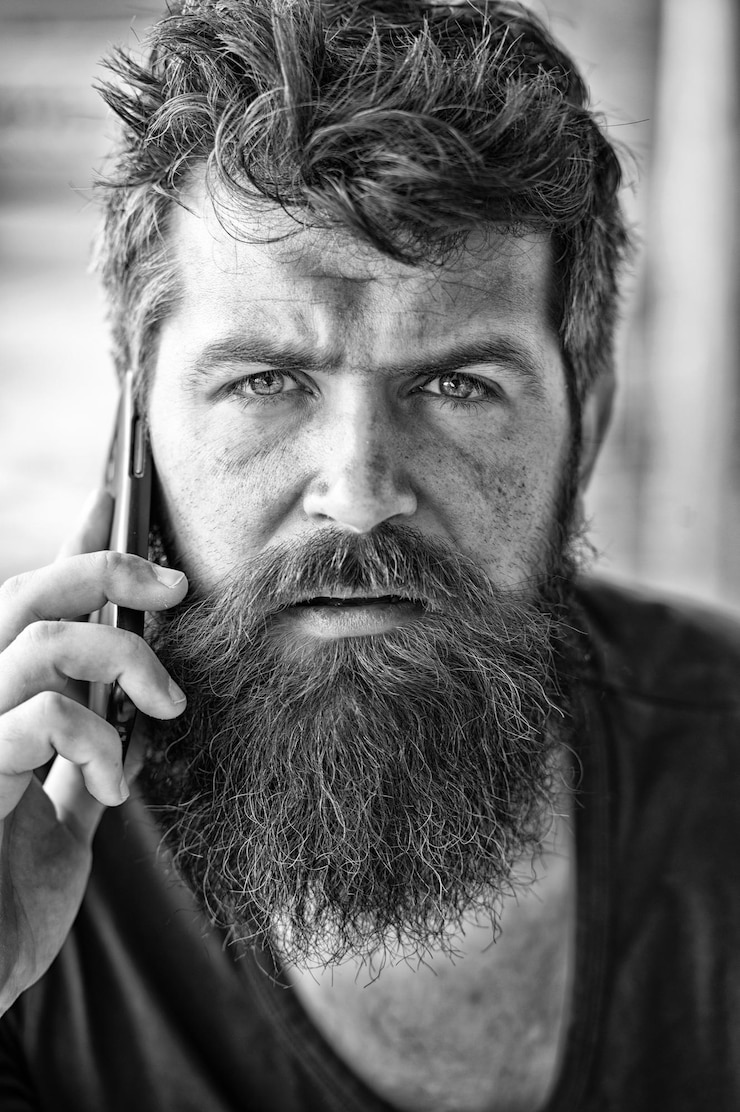 Foto hipster barbudo comunicar chamada de smartphone comunicação móvel conceito de comunicação homem com barba e bigode conversa de celular fundo desfocado homem barbudo segura celular