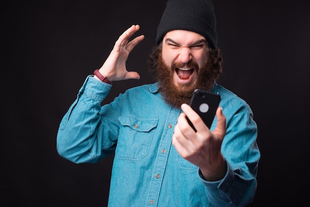 Hipster barbudo furioso gritando no smartphone e gesticulando