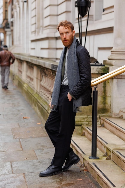 Hipster barbudo se inclina contra uma grade no meio de uma rua de londres