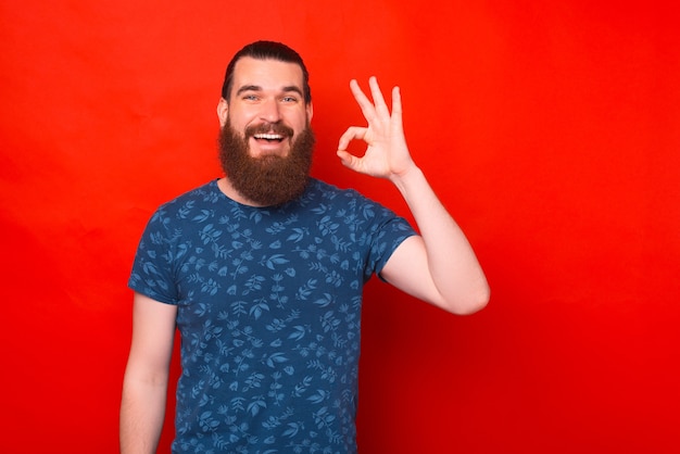 Hipster barbudo vestindo uma camiseta azul está mostrando um gesto de ok.