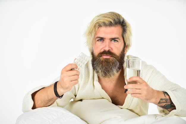 Hipster beber água tomar remédios Dor de cabeça ressaca Remédio para ressaca Perder a noite de sono é uma experiência bastante comum para os jovens Conceito de ressaca Cara dolorida do homem acordando de manhã