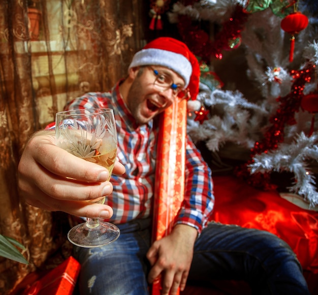 Hipster borracho con copa de champán bajo el árbol de Navidad. Año nuevo. Humor navideño.