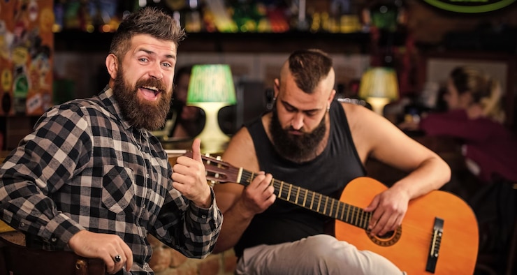 Foto hipster brutal barbudo com amigo no pub homem toca violão no pub amigos alegres cantam música de guitarra relaxamento no pub amigos relaxando no pub concerto de música ao vivo performance acústica no pub