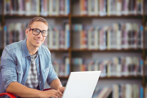 Hipster en la computadora portátil contra los libros en el escritorio de la biblioteca