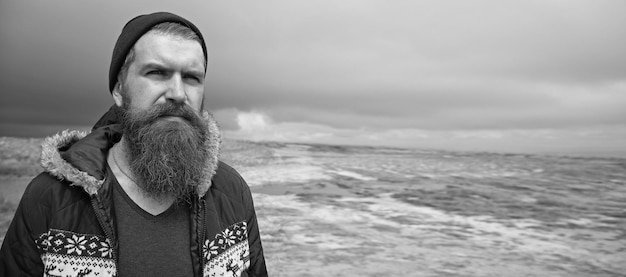 Hipster de homem bonito ou cara com barba e bigode na cara séria no chapéu e jaqueta ao ar livre no topo da montanha contra o céu nublado em fundo natural, copie o espaço