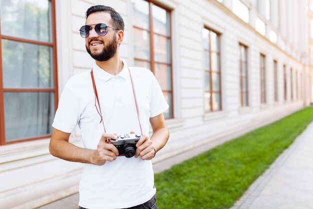 Hipster elegante com barba e câmera, andando pela cidade com uma câmera,