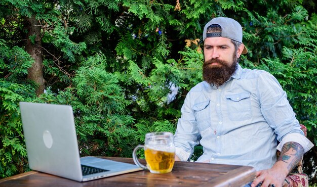 Hipster entspannt sitzen Terrasse im Freien mit Bier Bärtiger Hipster Freiberufler genießen Feierabend mit Bierkrug Er verdient dieses Pint Brutaler Mann Freizeit mit Bier und Online-Spiel Endlich Freitag