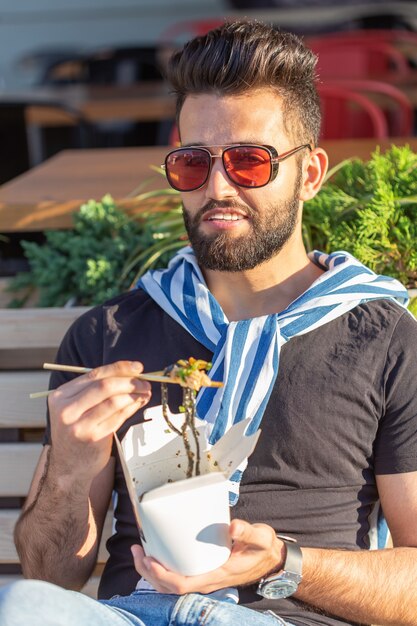 Hipster está comiendo fideos chinos con palillos de madera