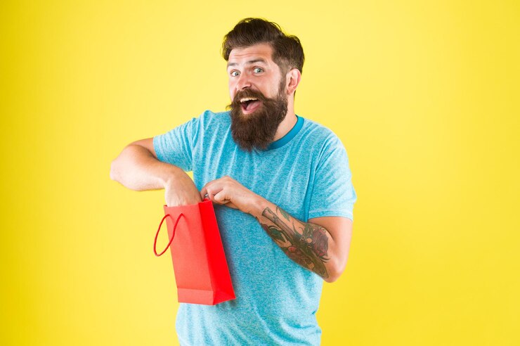 Foto hipster feliz segura saco de papel homem barbudo sorrindo com compra compra por impulso conceito de compra loja boutique de shopping comprar produto aspectos podem influenciar o comportamento de tomada de decisão do cliente