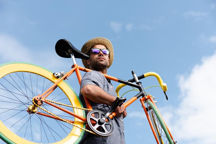 Hipster hispano que lleva una bicicleta fija colorida en su hombro con un cielo azul como fondo
