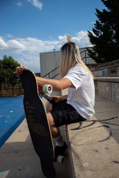 Hipster irreconhecível com cabelo comprido e longboard sentado nos degraus conversando ao telefone celular