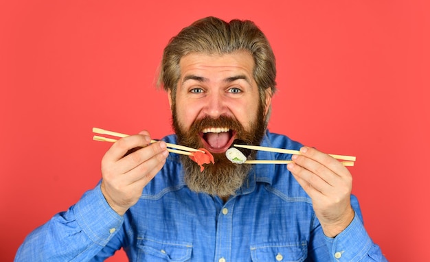 Hipster isst Sushi mit Stäbchen leckere Sushi-Rolle traditionelles und gesundes Essen in Japan japanisches Sushi-Gericht Mann isst traditionelles japanisches Essen mit Stäbchen Abendessen zu Hause