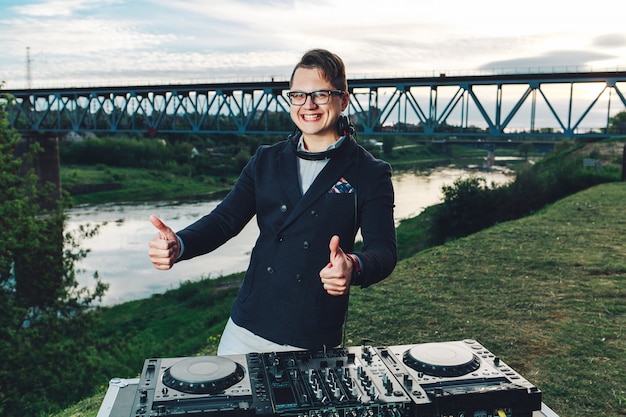 Hipster jovem em um terno azul com fones de ouvido levanta os dedos