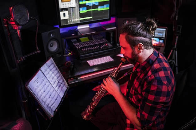 Hipster con joven está tocando un instrumento musical con composición en el estudio para grabar su nueva canción.