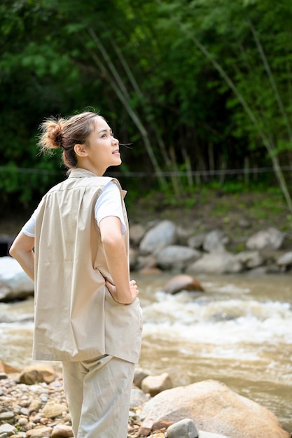 Hipster joven mujer asiática de pie cerca del río mirando la hermosa vista