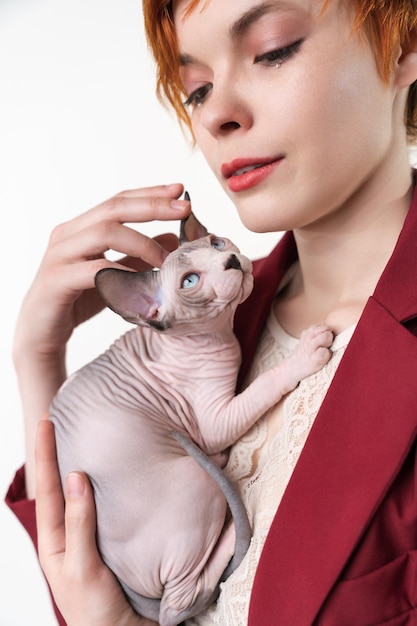 Hipster joven pelirroja mujer con pelo corto abrazando suavemente a su pecho Gato Sphynx canadiense