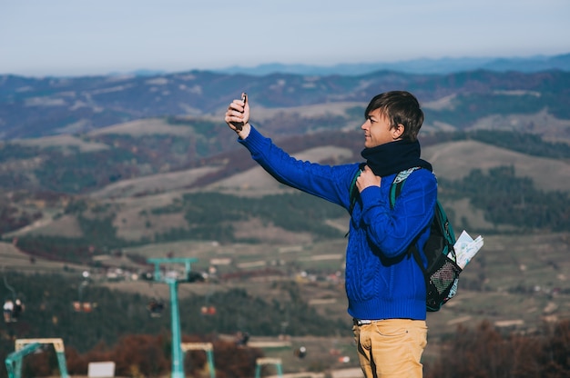 Hipster joven que toma la foto por teléfono inteligente en el pico de la montaña