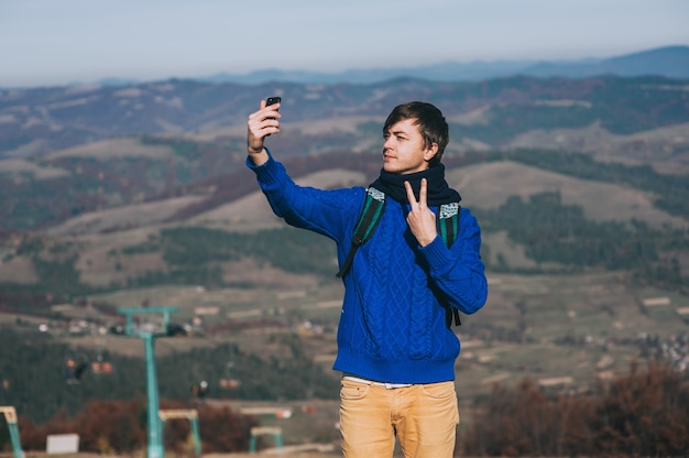 Hipster joven que toma la foto por teléfono inteligente en el pico de la montaña