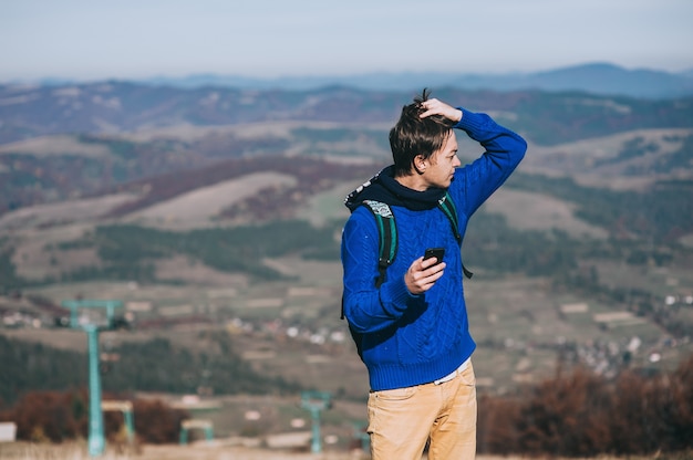 Hipster joven que toma la foto por teléfono inteligente en el pico de la montaña