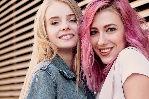 Hipster junge erwachsene Freunde umarmen sich beim Abhängen in der Stadt. Zwei junge Frauen lachen und gehen und genießen einen unbeschwerten Urlaubslebensstil