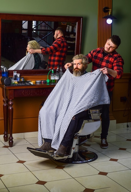 Hipster-Kunde bekommt Haarschnitt Friseur und Friseur widmen sich der Aufgabe, Sie besser aussehende Person zu machen Friseur mit Schere und Kunde Friseur arbeitet an Frisur für bärtigen Mann Barbershop-Hintergrund