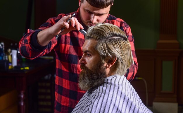 Hipster-Kunde bekommt Haarschnitt Friseurschere Verwalten Sie Ihre Erwartungen Schneiden Sie Haare Friseur, der Frisur für bärtigen Mann herstellt Barbershop-Hintergrund Kerl mit langem, gefärbtem blondem Haar, Nahaufnahme, Rückansicht