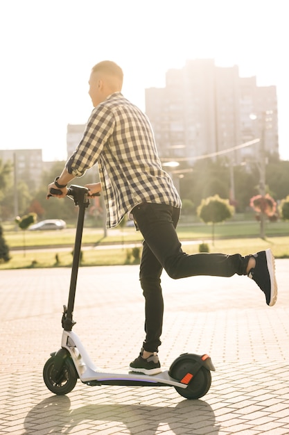 Foto hipster-mann, der auf einem elektroroller durch die stadt zur arbeit pendelt. umweltfreundlicher transport. elektrotransport mit hoher geschwindigkeit. mann, der einen escooter reitet. ökologie und urbaner lebensstil