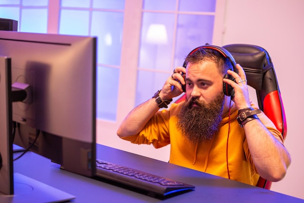 Hipster-Mann, der professionelle Videospiele in seinem Zimmer mit bunten Neonlichtern spielt. Mann mit Kopfhörern beim Spielen von Videospielen.