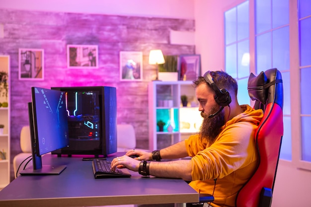 Hipster-Mann, der professionelle Videospiele in seinem Zimmer mit bunten Neonlichtern spielt. Mann mit Kopfhörern beim Spielen von Videospielen.