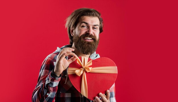 Hipster masculino barbudo em camisa quadriculada segura amor de presente de caixa de coração