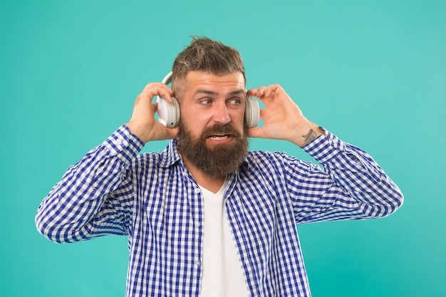 Hipster masculino maduro não suporta volume de música alta no fone de ouvido no fundo azul, volume.