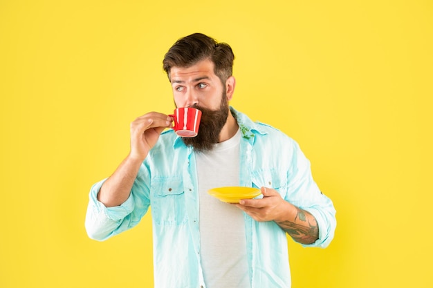 Hipster mit Bart hält Kaffeetasse auf gelbem Hintergrund, Morgen