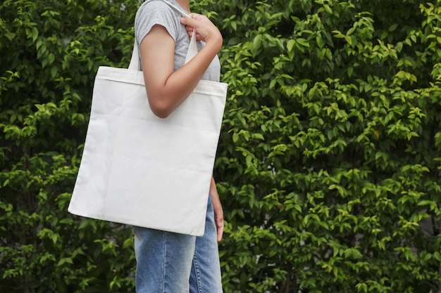 Hipster mujer con bolsa de algodón blanco sobre fondo de hoja verde