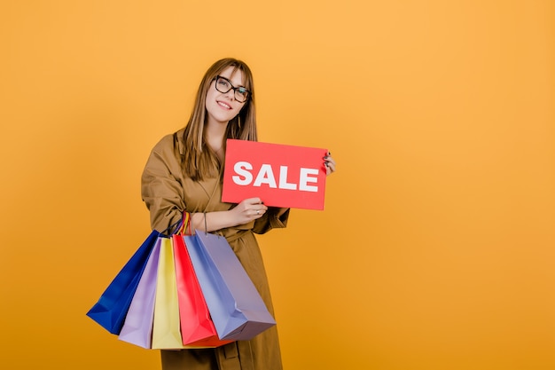 Hipster mujer en otoño gabardina y gafas con cartel de venta y coloridos bolsos de compras