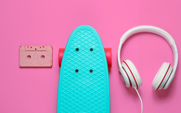 Hipster-Outfit. Skateboard mit Kopfhörern, Audiokassette auf rosa Hintergrund